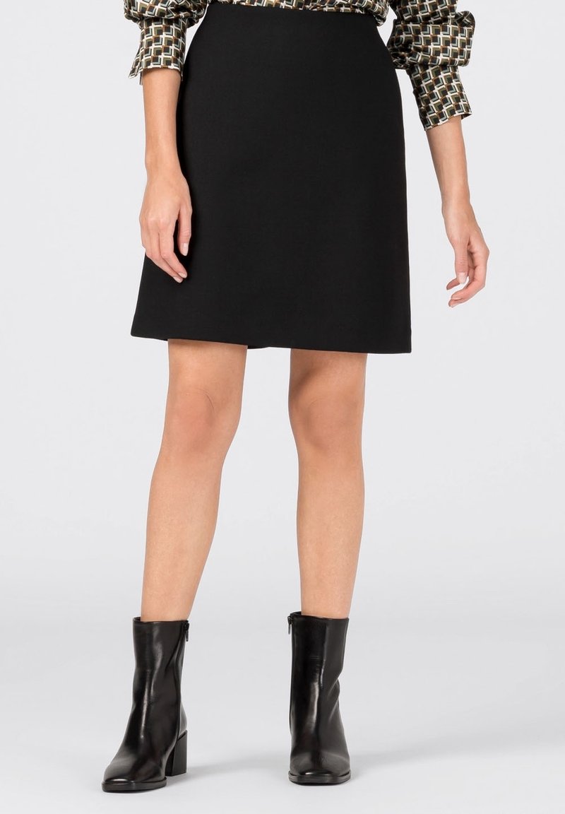 Black A-line skirt, made of smooth fabric. Worn with a patterned blouse. Paired with glossy black ankle boots. Simple design, no visible embellishments.