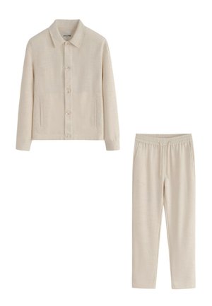 Veste beige boutonnée avec col et poches, associée à un pantalon assorti avec taille élastique et cordon de serrage.