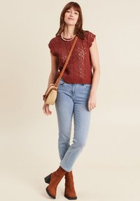 Top lavorato a maglia color ruggine, jeans azzurri chiari e stivali con tacco marroni. Accessoriato con una piccola borsa a tracolla. Design semplice con trama in pizzo.