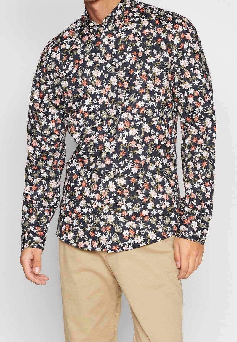 Chemise à manches longues florale en bleu marine foncé avec des fleurs blanches, roses et orange. Col boutonné et tissu à texture lisse.