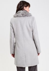 Abrigo de lana gris con cuello de piel sintética, mangas largas y un corte ajustado, con un diseño limpio en la parte posterior y sin cierres visibles.