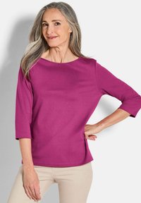 Fuchsia-kleurige top met een relaxte pasvorm, 3/4 mouwen en een ronde halslijn. Gemaakt van zachte stof met zijsplitten voor extra comfort.