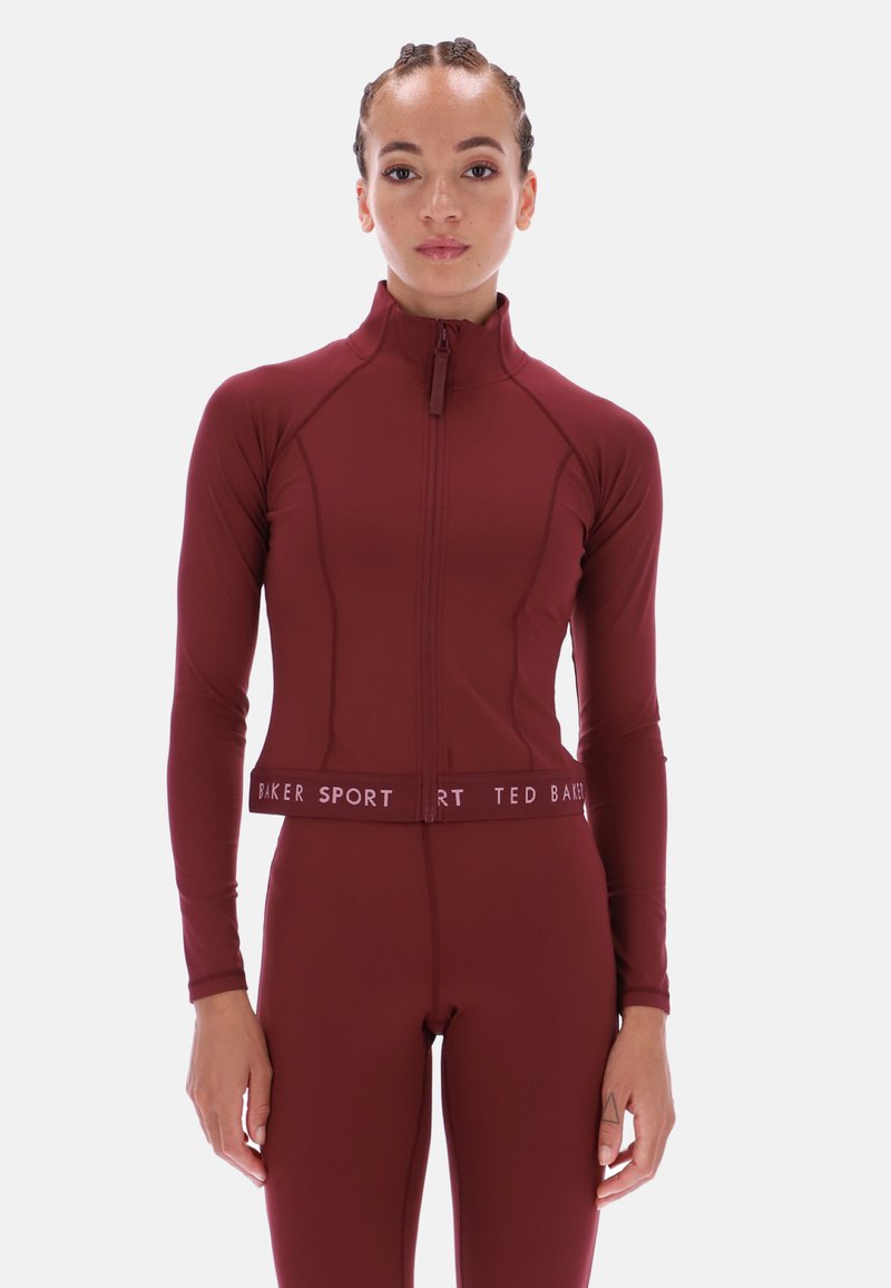 Vīnsarkanā sporta jaka ar rāvējslēdzēja aizdari, garām piedurknēm un piegulošu siluetu. Izceļas ar kontrastējošu baltu "BAKER SPORT" joslu viduklī.