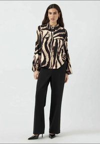 Long-sleeve, silk blouse with a cream and black abstract pattern, paired with black tailored trousers and pointed black heels.