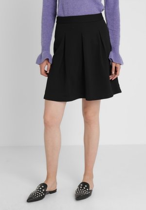 Sort knælang nederdel med plisseringer ved taljen. Lavet af et glat stof. Kombineret med sorte slip-on sko med sølvnitter.