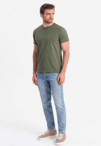 Oliven grøn bomulds t-shirt med rund halsudskæring, parret med lyseblå denim jeans og beige sneakers med hvide såler og snørebånd.