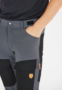 Grå och svarta arbetsbyxor med en blandning av material, dragkedjefickor och en läderlogotyp på låret.