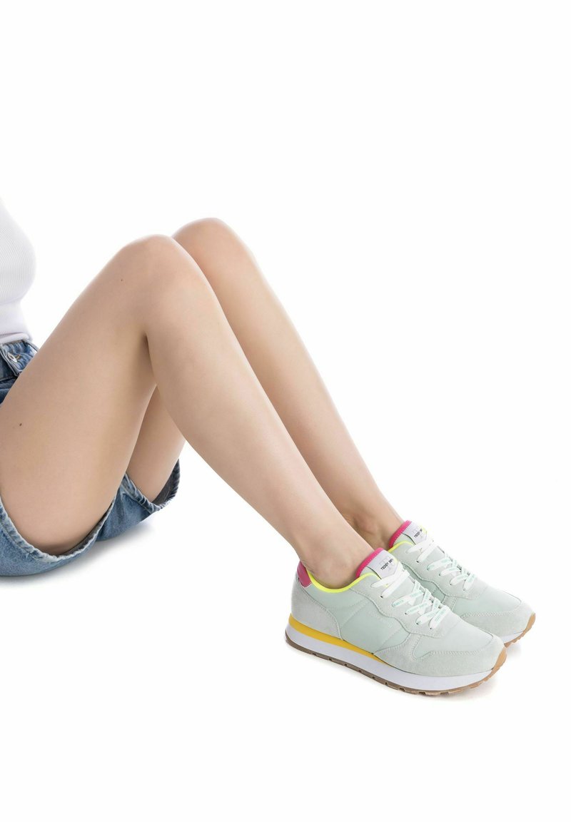 Baskets bleu clair avec des surfaces texturées, lacets blancs, et un accent rose et jaune sur le talon et la semelle. Semelle en caoutchouc avec motif.