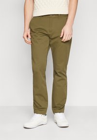 Chinos verde oliva in cotone, con design a gamba dritta, tasche frontali e chiusura con bottone, abbinati a sneaker bianche.