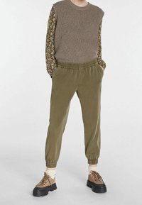 Olivegrønne joggingbukser med elastiske manchetter, parret med en ribbet brun top med lange ærmer i blomsterprint. Brune snørebåndssko fuldender udseendet.
