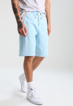 Hellblaue Baumwollshorts mit elastischem Bund und Kordelzug, die knapp über dem Knie enden, kombiniert mit weißen Turnschuhen.