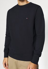 Felpa girocollo blu navy in cotone, con polsini e orlo a coste, e un piccolo logo rosso, bianco e blu sul petto.