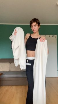 Witte fuzzy sweatshirt met lange mouwen in de linkergreep en bijpassende witte sweatpants in de rechtergreep, weergegeven tegen een groene achtergrond.