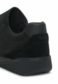 Czarne zamszowe sneakersy z gładkim teksturowanym piętą, kontrastującymi matowymi czarnymi akcentami i amortyzowaną gumową podeszwą. Zawierają subtelną szczegółową logo.