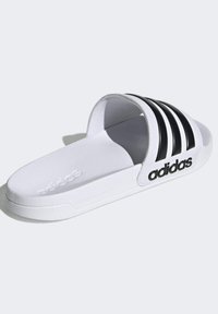 Adidas sandaler i hvit med svarte tre striper og logo. Teksturerte såler, flat såle og åpen tådesign. Cloudfoam polstring.