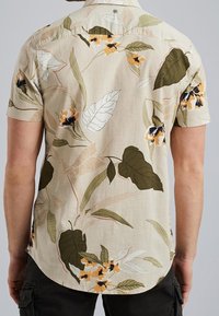 Kortærmet skjorte lavet af let stof, med en beige baggrund prydet af grønne og gule blomstermønstre samt diskrete hvide bladkonturer.