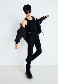 Giacca nera imbottita sopra una canotta nera, abbinata a jeans neri e sneakers nere. Gli accessori includono occhiali da sole neri.