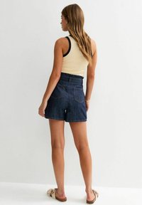 Denim shorts with a high waist, dark blue color, and five pockets, paired with a sleeveless cream top featuring navy accents.