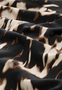 Tessuto nero con un motivo astratto stampato in crema e marrone, che presenta una texture liscia e pieghe ondulate.