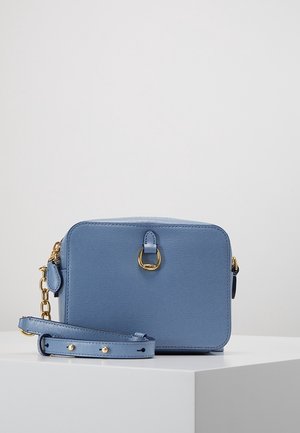 Mała prostokątna niebieska skórzana torba na ramię z złotym okuciem i regulowanym paskiem, leżąca na białej powierzchni.