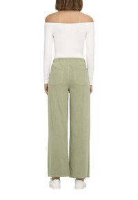 Pantaloni larghi verdi con vita elasticizzata, dotati di tasche posteriori, abbinati a un top bianco aderente a spalle scoperte e sneakers bianche.