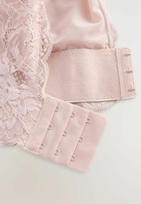 Sezione di reggiseno in pizzo rosa caratterizzata da delicato pizzo floreale, materiale in rete liscia, chiusure regolabili con ganci e asole, e texture morbide.