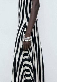 Black and white striped dress with a fitted bodice and a flared skirt, featuring a smooth silver bangle on a dark hand.