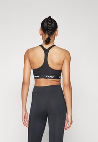 Sutien desportivo preto com design de costas em V e logotipo branco da DKNY na faixa, usado com leggings pretas combinando, visto de trás.