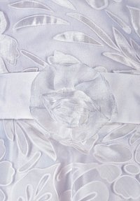 Bílá vyšívaná látka s květinovými vzory, s páskem ze saténu a dekorativním saténovým květinovým akcentem v pase.