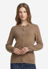 Brun cardigan gjord av mjukt stickat tyg, med rund halsringning, knappstängning framtill och långa ärmar. Ribbad mudd och nederkant.