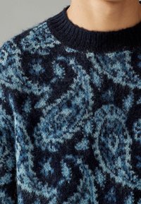 Pullover-Pullover mit einem navyblauen und petrolfarbenen Paisleymuster, hergestellt aus weichem, flauschigem Material mit einem gerippten Rundhalsausschnitt.
