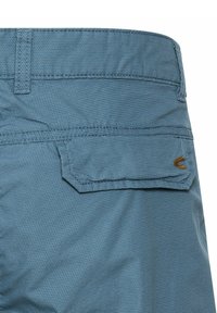 Lyseblå shorts lavet af tekstureret stof, med en baglomme med vinklet klap og en lille brun logo detalje.