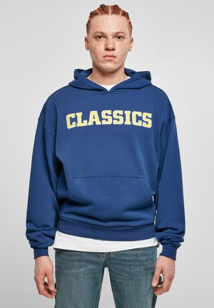 Hanorac albastru dintr-un material moale, cu un buzunar în față. Prezintă textul "CLASSICS" în litere îngroșate galbene pe piept. Croială casual, cu mansete din material ribbed.