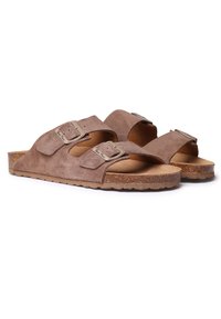 Sandales à glissière en suede marron avec deux sangles réglables, boucles en métal et une semelle en liège naturel. Semelle en caoutchouc texturé pour une meilleure adhérence.