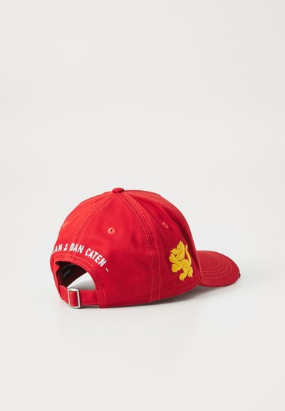 Röd basebollkeps av bomulls-twill. Har en broderad gullejon och vit text "DSQUARED2" på baksidan. Justerbar rem ingår.