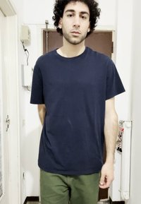 T-shirt de algodão azul marinho com decote redondo e mangas curtas, combinada com calças verde-oliva. Design simples, sem padrões ou logótipos visíveis.