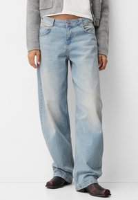 Light blue wide-leg jeans with a faded texture, five-pocket design, and a button closure, paired with dark shoes.