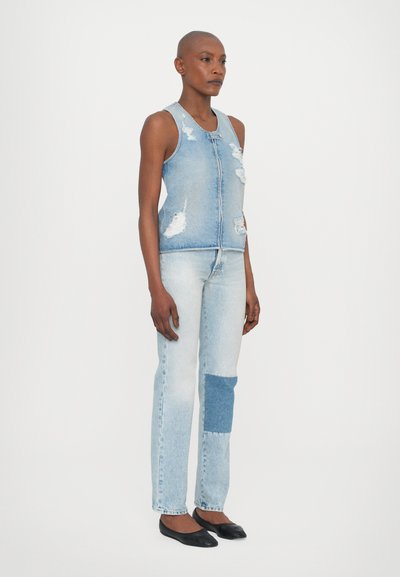 Denimist vest, millel on kulunud detailid ja esine lukustus, kombineeritud helesiniste teksadega, millel on ühe jala peal denimipatch ja sirge lõige.