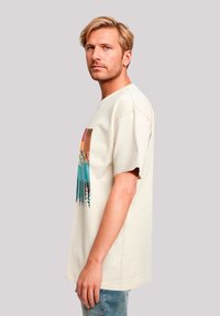 Korte mouwen beige katoenen T-shirt met een kleurrijk grafisch ontwerp van bergen en bomen in blauwe en oranje tinten.