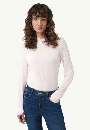 Langärmliges pinkes Oberteil aus glattem Stoff mit einem hohen Kragen, kombiniert mit dunkelblauen Jeans mit einer Tasche und Knopf.
