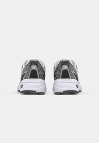 Par de zapatillas deportivas gris y blancas con detalles en negro, vistas desde atrás sobre un fondo blanco liso.