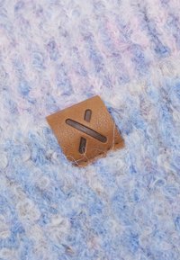 Tessuto blu e dai toni pastello con un aspetto peloso; presenta un'etichetta in cuoio marrone con un design a croce in rilievo.