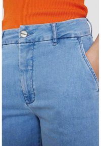 Gaiši zili denima džinsi ar maigu nolietotu tekstūru. Iespējamie elementi ir sudraba poga un priekšējā kabata, izšūtas vīles un augsta josta.