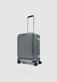 Silberner Hartschalen-Koffer mit vertikalen Rillen, ausziehbarem Griff, vier schwarzen Rollen und einem schlanken Design. Glatte metallische Oberfläche.