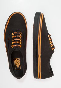 Baskets en toile noires avec des accents orange vif, dotées de lacets contrastés, de semelles en caoutchouc et d'un design classique à profil bas.