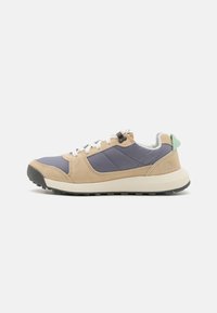 Die Sneaker besitzen ein oberes Material aus beigem Wildleder und blauer Synthetik, mit weißen Schnürsenkeln, einer hellgrünen Fersenkappe und einer klobigen schwarzen Gummisohle.