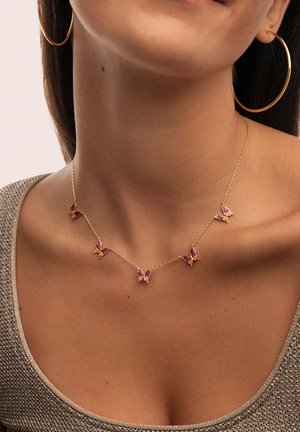 Collar de oro con cinco colgantes de mariposa con detalles en púrpura y naranja, llevado en un cuello desnudo sobre una blusa gris texturizada.