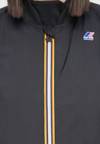 K-Way svart vindjakke med høy krage, med en sentral multicolor stripete glidelås og logo på venstre bryst.