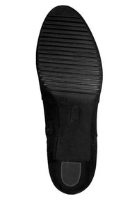 Suela de zapato de goma negra con patrón estriado para tracción, que presenta una puntera redonda y suave y una pequeña área elevada cerca del talón.