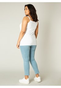 Witte mouwloze top gecombineerd met lichtblauwe skinny jeans. De jeans hebben een ruwe zoom en worden aangevuld met witte sneakers.